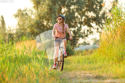 Image of Joyful young woman riding a bicycle at the riverside and meadow promenade