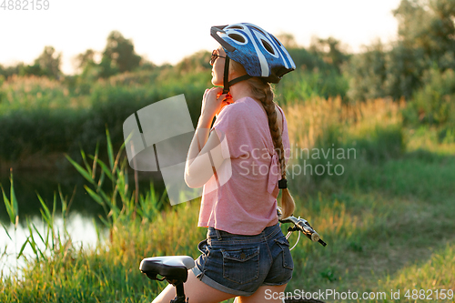 Image of Joyful young woman riding a bicycle at the riverside and meadow promenade