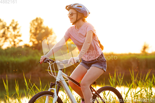 Image of Joyful young woman riding a bicycle at the riverside and meadow promenade