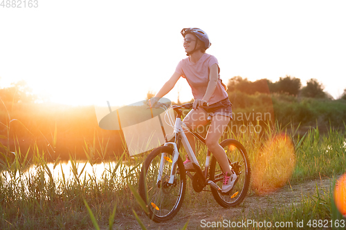 Image of Joyful young woman riding a bicycle at the riverside and meadow promenade