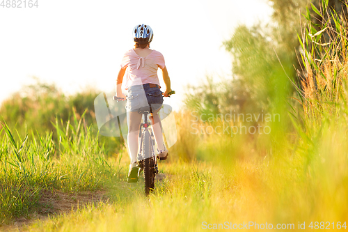 Image of Joyful young woman riding a bicycle at the riverside and meadow promenade