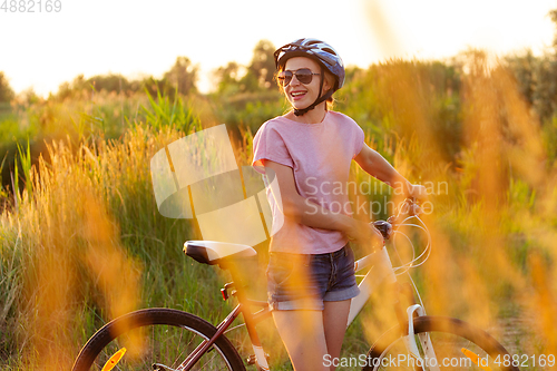 Image of Joyful young woman riding a bicycle at the riverside and meadow promenade