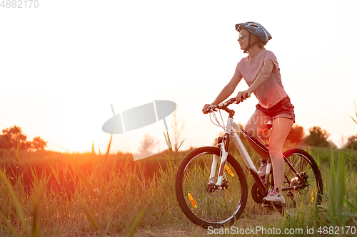 Image of Joyful young woman riding a bicycle at the riverside and meadow promenade