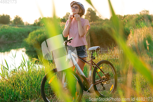 Image of Joyful young woman riding a bicycle at the riverside and meadow promenade