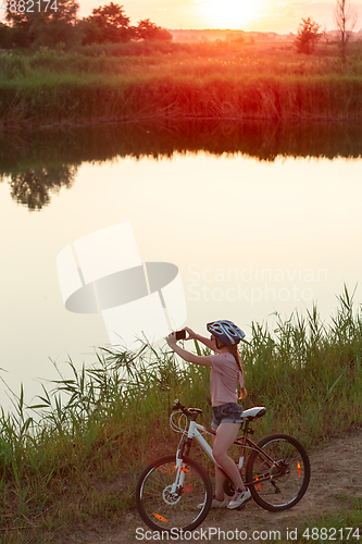 Image of Joyful young woman riding a bicycle at the riverside and meadow promenade
