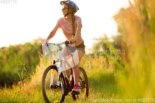 Image of Joyful young woman riding a bicycle at the riverside and meadow promenade