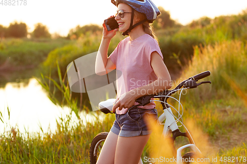 Image of Joyful young woman riding a bicycle at the riverside and meadow promenade