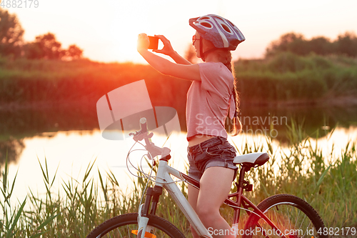 Image of Joyful young woman riding a bicycle at the riverside and meadow promenade