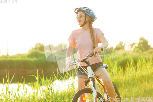 Image of Joyful young woman riding a bicycle at the riverside and meadow promenade