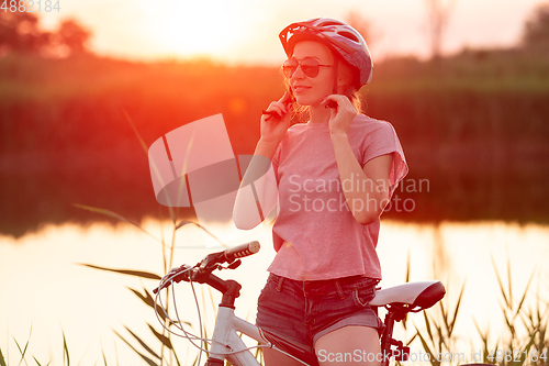 Image of Joyful young woman riding a bicycle at the riverside and meadow promenade