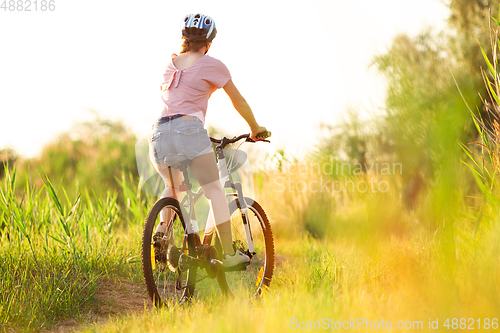 Image of Joyful young woman riding a bicycle at the riverside and meadow promenade