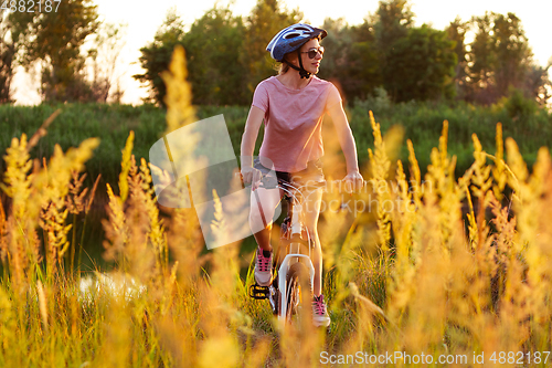 Image of Joyful young woman riding a bicycle at the riverside and meadow promenade