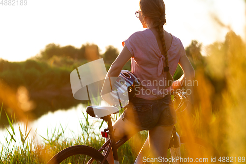 Image of Joyful young woman riding a bicycle at the riverside and meadow promenade