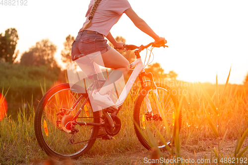 Image of Joyful young woman riding a bicycle at the riverside and meadow promenade