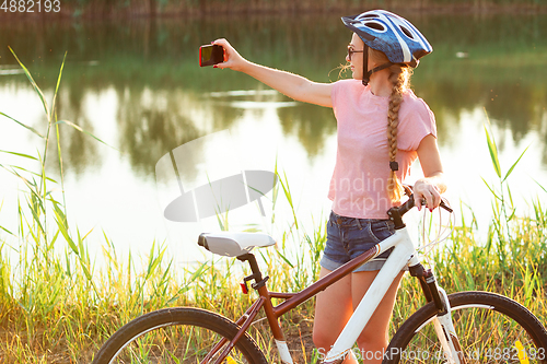 Image of Joyful young woman riding a bicycle at the riverside and meadow promenade