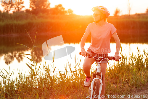 Image of Joyful young woman riding a bicycle at the riverside and meadow promenade