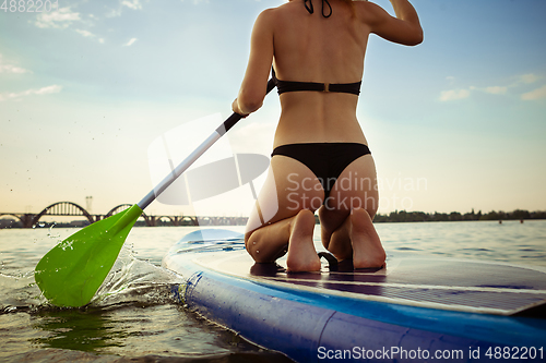 Image of Young attractive woman sitting on paddle board, SUP. Active life, sport, leisure activity concept