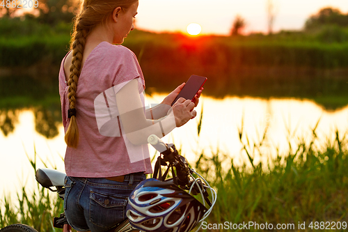 Image of Joyful young woman riding a bicycle at the riverside and meadow promenade