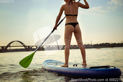 Image of Young attractive woman standing on paddle board, SUP. Active life, sport, leisure activity concept