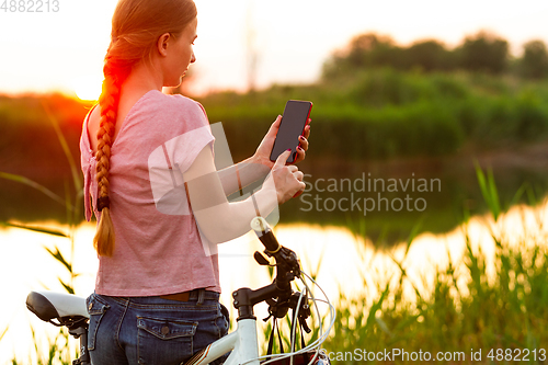 Image of Joyful young woman riding a bicycle at the riverside and meadow promenade