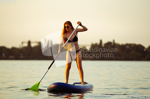 Image of Young attractive woman standing on paddle board, SUP. Active life, sport, leisure activity concept