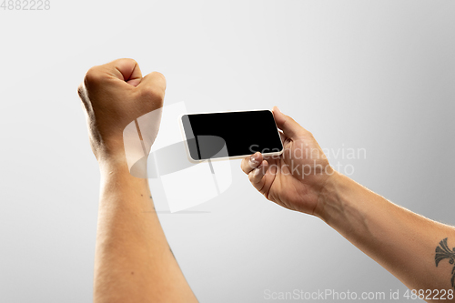Image of Close up male hands holding phone with blank screen during online watching of popular sport matches and championships all around the world. Copyspace for ad