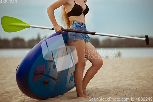 Image of Young attractive woman standing next to paddle board, SUP. Active life, sport, leisure activity concept