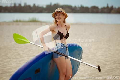 Image of Young attractive woman standing next to paddle board, SUP. Active life, sport, leisure activity concept