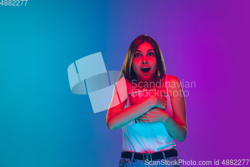 Image of Caucasian young woman\'s portrait isolated on gradient purple-blue background in neon light, cinema, movie watching