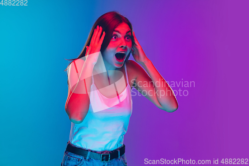 Image of Caucasian young woman\'s portrait isolated on gradient purple-blue background in neon light, cinema, movie watching