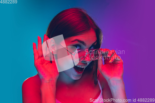 Image of Caucasian young woman\'s portrait isolated on gradient purple-blue background in neon light, cinema, movie watching