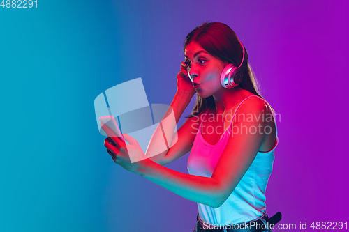 Image of Caucasian young woman\'s portrait isolated on gradient purple-blue background in neon light