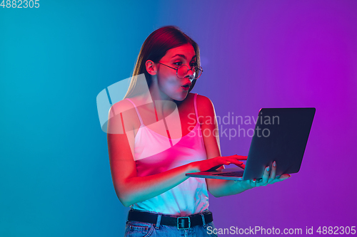 Image of Caucasian young woman\'s portrait isolated on gradient purple-blue background in neon light, cinema, movie watching