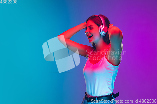 Image of Caucasian young woman\'s portrait isolated on gradient purple-blue background in neon light