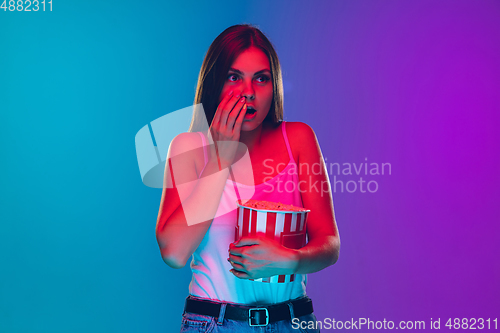 Image of Caucasian young woman\'s portrait isolated on gradient purple-blue background in neon light, cinema, movie watching