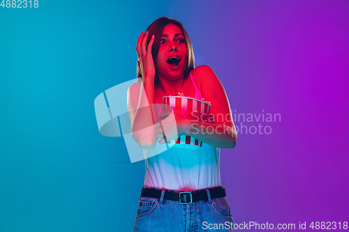 Image of Caucasian young woman\'s portrait isolated on gradient purple-blue background in neon light, cinema, movie watching