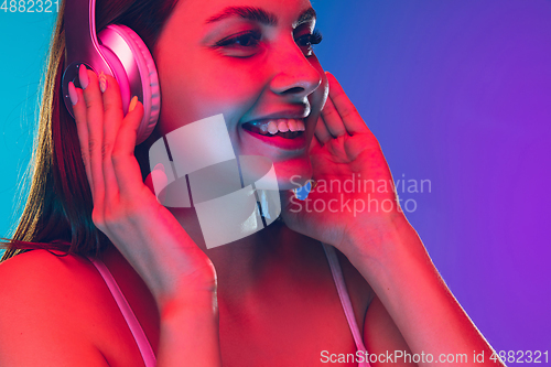 Image of Caucasian young woman\'s portrait isolated on gradient purple-blue background in neon light