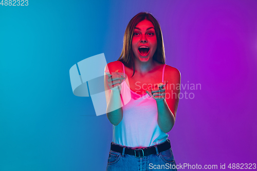 Image of Caucasian young woman\'s portrait isolated on gradient purple-blue background in neon light, cinema, movie watching