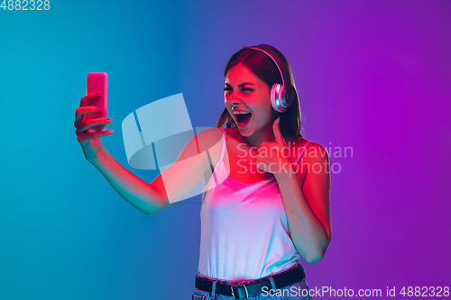 Image of Caucasian young woman\'s portrait isolated on gradient purple-blue background in neon light