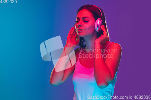 Image of Caucasian young woman\'s portrait isolated on gradient purple-blue background in neon light