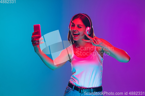 Image of Caucasian young woman\'s portrait isolated on gradient purple-blue background in neon light