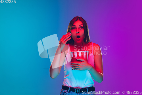 Image of Caucasian young woman\'s portrait isolated on gradient purple-blue background in neon light, cinema, movie watching