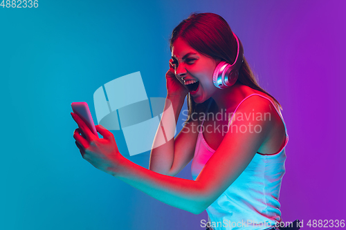 Image of Caucasian young woman\'s portrait isolated on gradient purple-blue background in neon light