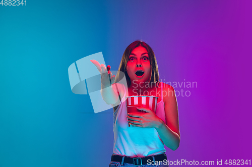 Image of Caucasian young woman\'s portrait isolated on gradient purple-blue background in neon light, cinema, movie watching