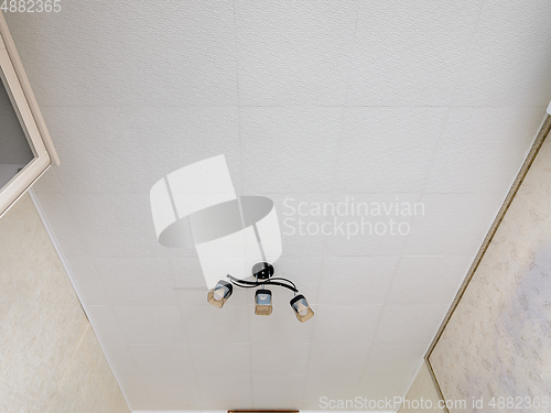 Image of A fragment of the interior, a view of a modest ceiling with glued ceiling tiles and a small chandelier