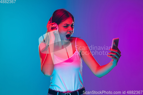 Image of Caucasian young woman\'s portrait isolated on gradient purple-blue background in neon light