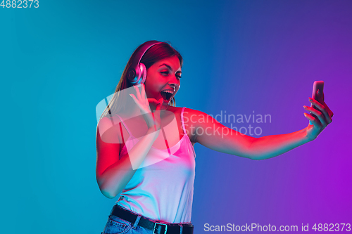Image of Caucasian young woman\'s portrait isolated on gradient purple-blue background in neon light