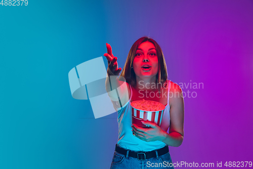 Image of Caucasian young woman\'s portrait isolated on gradient purple-blue background in neon light, cinema, movie watching