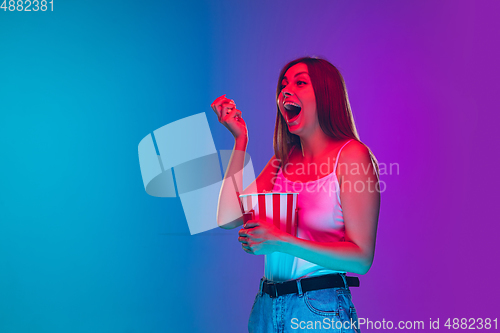 Image of Caucasian young woman\'s portrait isolated on gradient purple-blue background in neon light, cinema, movie watching