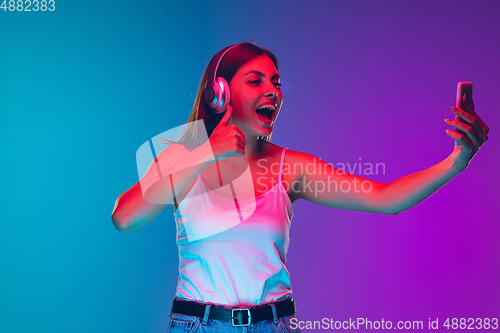 Image of Caucasian young woman\'s portrait isolated on gradient purple-blue background in neon light